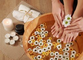 Woman putting feet in wooden basin with water and small flowers for making pedicure