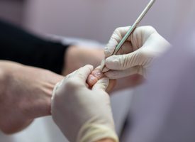 Closeup of professional pedicurist making medical pedicure wearing protective gloves.